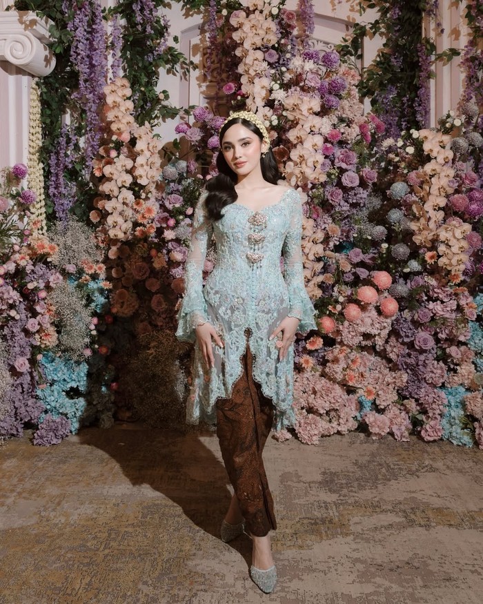Pada momen siraman, Syifa Hadju tampil lembut dalam kebaya bernuansa biru langit rancangan Didiet Maulana. Sentuhan modern dan tradisional berpadu melalui detail payet tujuh warna, pita dengan aksen tassel, serta kain batik bermakna doa dan harapan baik. Nuansa ini menciptakan kesan hangat dan personal, seolah membuka rangkaian cerita sebelum hari bahagia bersama El Rumi dimulai.